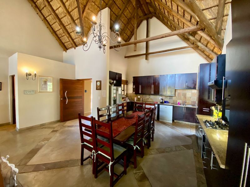 Spacious open-plan kitchen and dining area featuring a high vaulted thatched ceiling with exposed timber trusses and modern dark wood cabinetry.