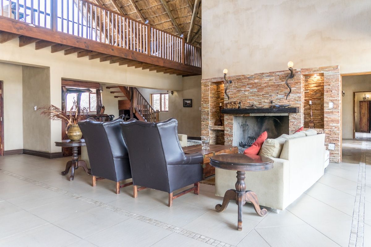 Spacious living room featuring a prominent stone-clad fireplace, high thatched ceilings, and a timber mezzanine level overlooking the main area.