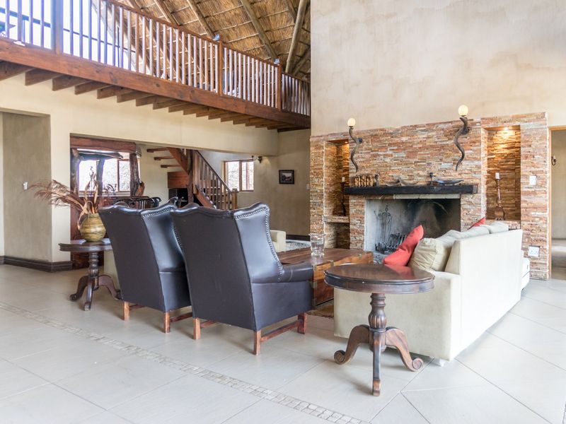 Spacious living room featuring a prominent stone-clad fireplace, high thatched ceilings, and a timber mezzanine level overlooking the main area.