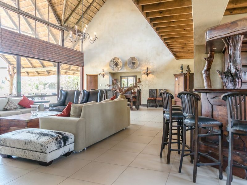 Spacious open-plan living area featuring a high vaulted thatched ceiling, exposed timber beams, tiled flooring, and a custom built-in bar.