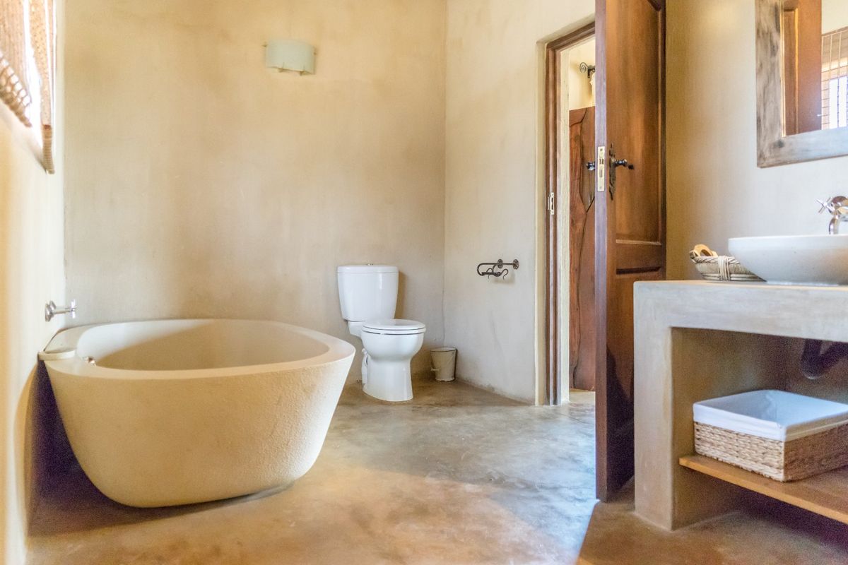 A rustic-style bathroom featuring a freestanding bathtub, concrete vanity with a vessel sink, and a wooden door.