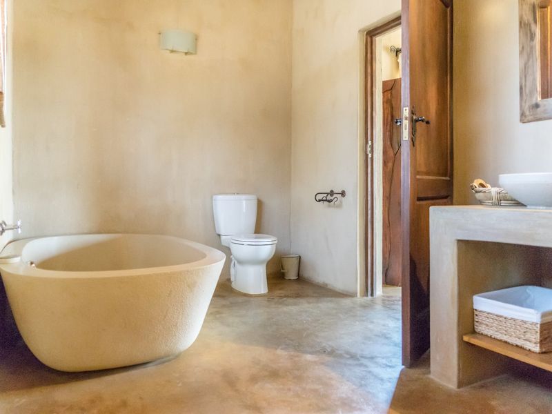 A rustic-style bathroom featuring a freestanding bathtub, concrete vanity with a vessel sink, and a wooden door.