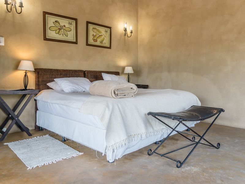A rustic-style bedroom featuring textured earth-toned walls, polished concrete flooring, and warm wall sconce lighting.