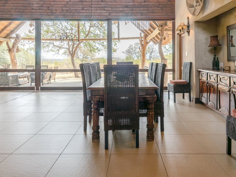 Spacious dining area featuring large format floor tiles, timber ceiling beams, and expansive glass sliding doors that open onto a covered outdoor patio.