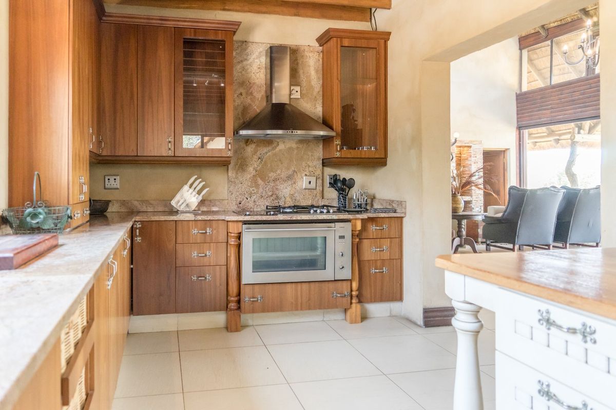 A well-appointed kitchen featuring warm wooden cabinetry, stone countertops, a stone backsplash, and integrated stainless steel appliances, flowing into an adjacent living area.