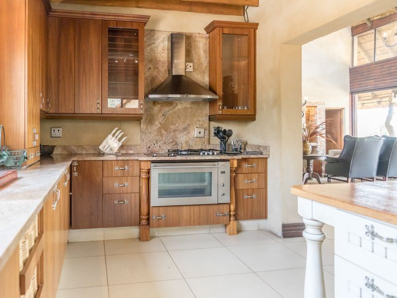 A well-appointed kitchen featuring warm wooden cabinetry, stone countertops, a stone backsplash, and integrated stainless steel appliances, flowing into an adjacent living area.