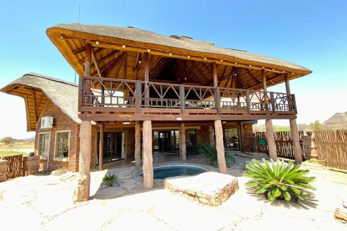 A spacious rear exterior view featuring a large thatched-roof balcony, stone patio, and a built-in plunge pool set within a natural landscape.