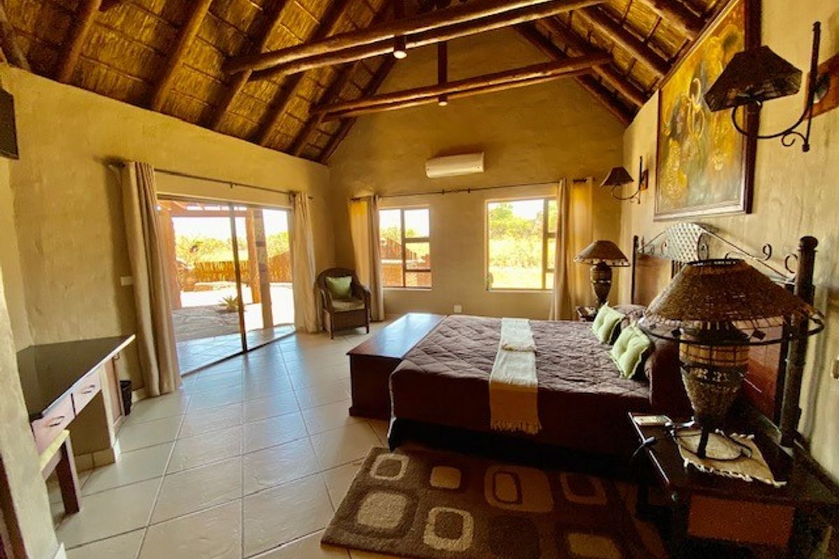 Spacious bedroom featuring a high vaulted thatched ceiling with exposed timber beams, tiled flooring, and direct access to an outdoor patio area.