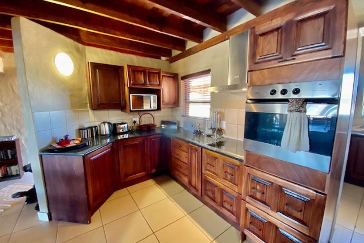 A functional kitchen featuring dark wood cabinetry, tiled flooring, exposed timber ceiling beams, and integrated stainless steel oven and extractor fan.