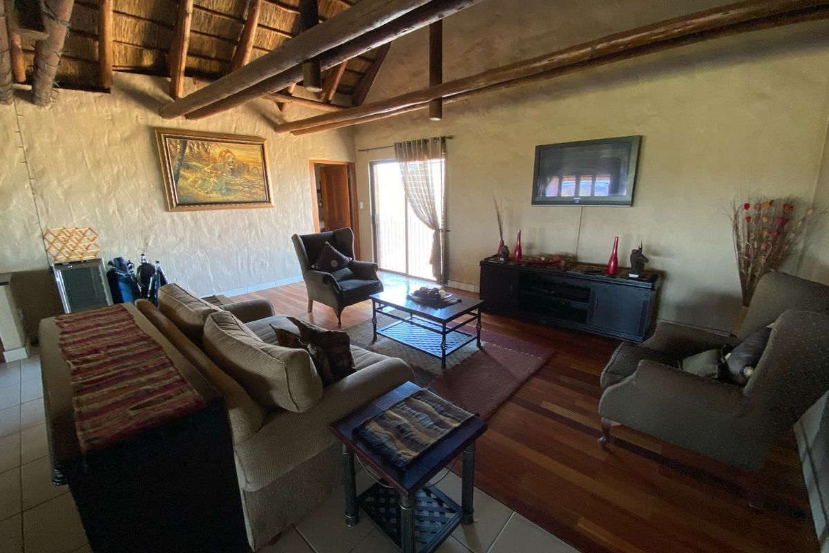 Spacious living room featuring a high vaulted thatched ceiling with exposed timber beams, textured walls, and a combination of tiled and hardwood flooring.