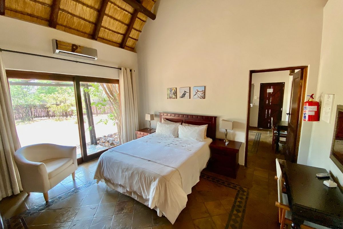 Spacious bedroom featuring a high vaulted thatched ceiling, tiled flooring, and large sliding glass doors providing direct access to the outdoor area.