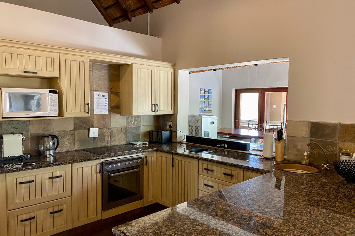 A functional kitchen featuring granite countertops, built-in oven, hob, and extractor fan, with a pass-through window overlooking the adjacent living area.