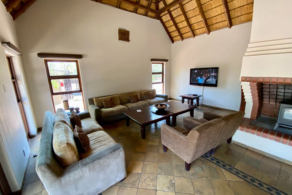 Spacious living room featuring a high vaulted thatched ceiling, exposed timber beams, stone tile flooring, and a built-in brick fireplace.