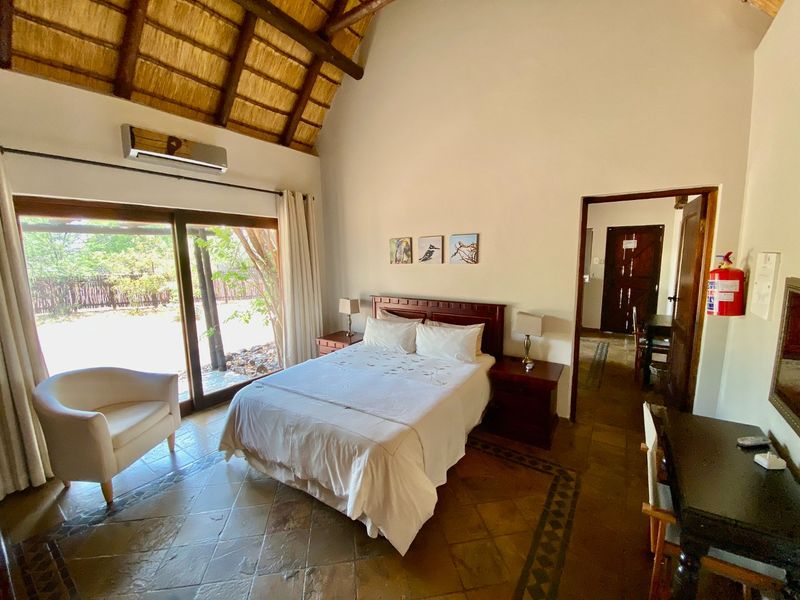 Spacious bedroom featuring a high vaulted thatched ceiling, tiled flooring, and large sliding glass doors providing direct access to the outdoor area.