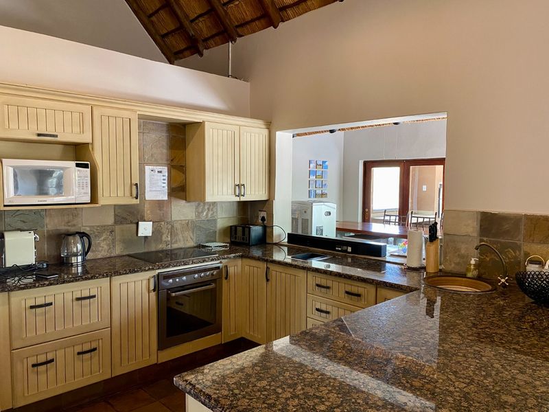 A functional kitchen featuring granite countertops, built-in oven, hob, and extractor fan, with a pass-through window overlooking the adjacent living area.