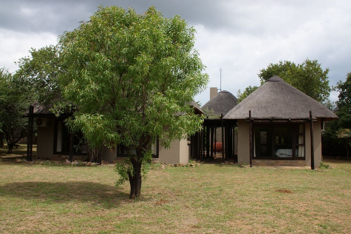 A view of the rear exterior of a property featuring traditional thatched roof structures and a spacious garden area.