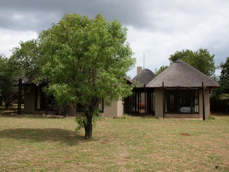 A view of the rear exterior of a property featuring traditional thatched roof structures and a spacious garden area.