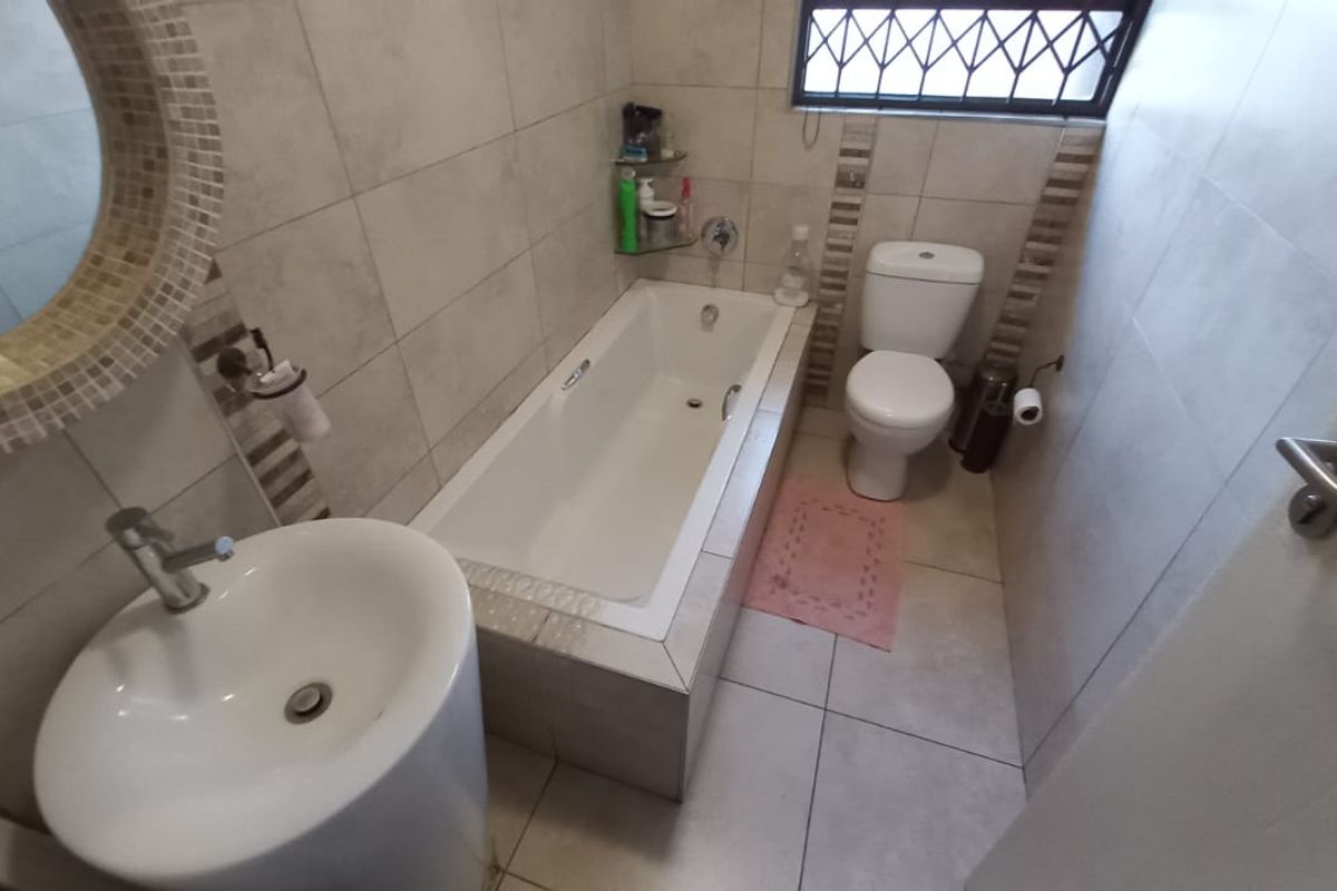 A compact bathroom featuring a built-in bathtub, pedestal sink, and toilet with neutral wall and floor tiling.