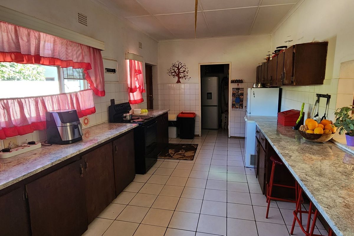 A functional kitchen featuring laminate countertops, dark wood cabinetry, tiled flooring, and a dedicated scullery area for additional storage and preparation.