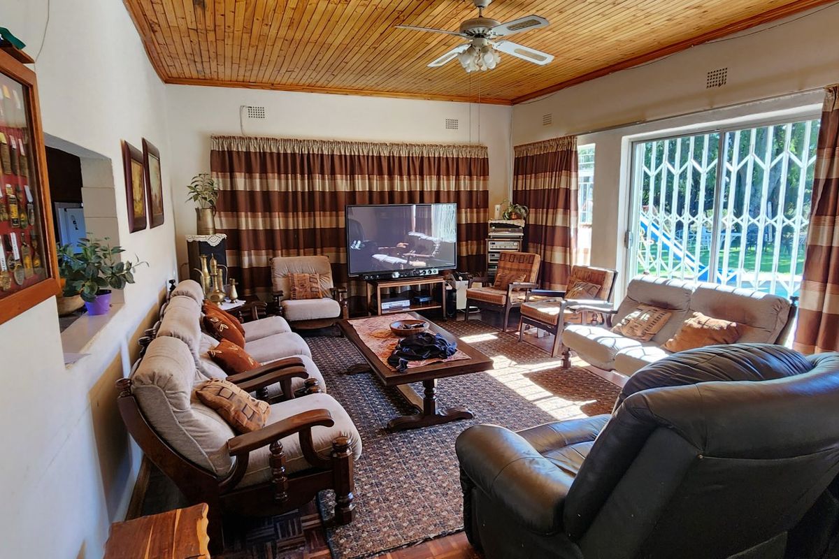 A spacious living room featuring a timber-clad ceiling, ceiling fan, and large sliding glass doors with security gates leading to the garden.