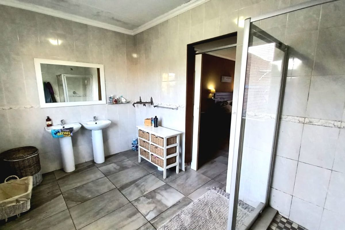 Spacious bathroom featuring dual pedestal sinks, a glass-enclosed shower, and full-height wall tiling.