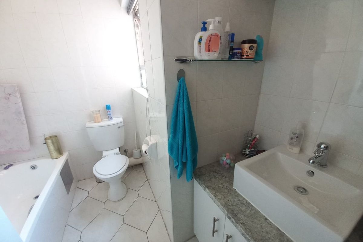 A functional bathroom featuring a bathtub, a vanity with a stone countertop, and a toilet, finished with white wall tiles and hexagonal floor tiles.