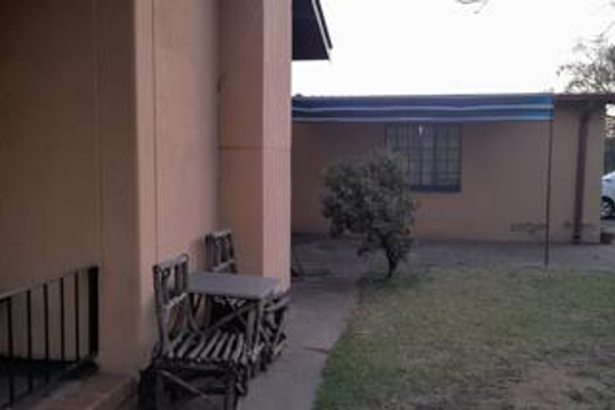 A view of the rear exterior area featuring a covered patio space, concrete pathway, and a small garden area.