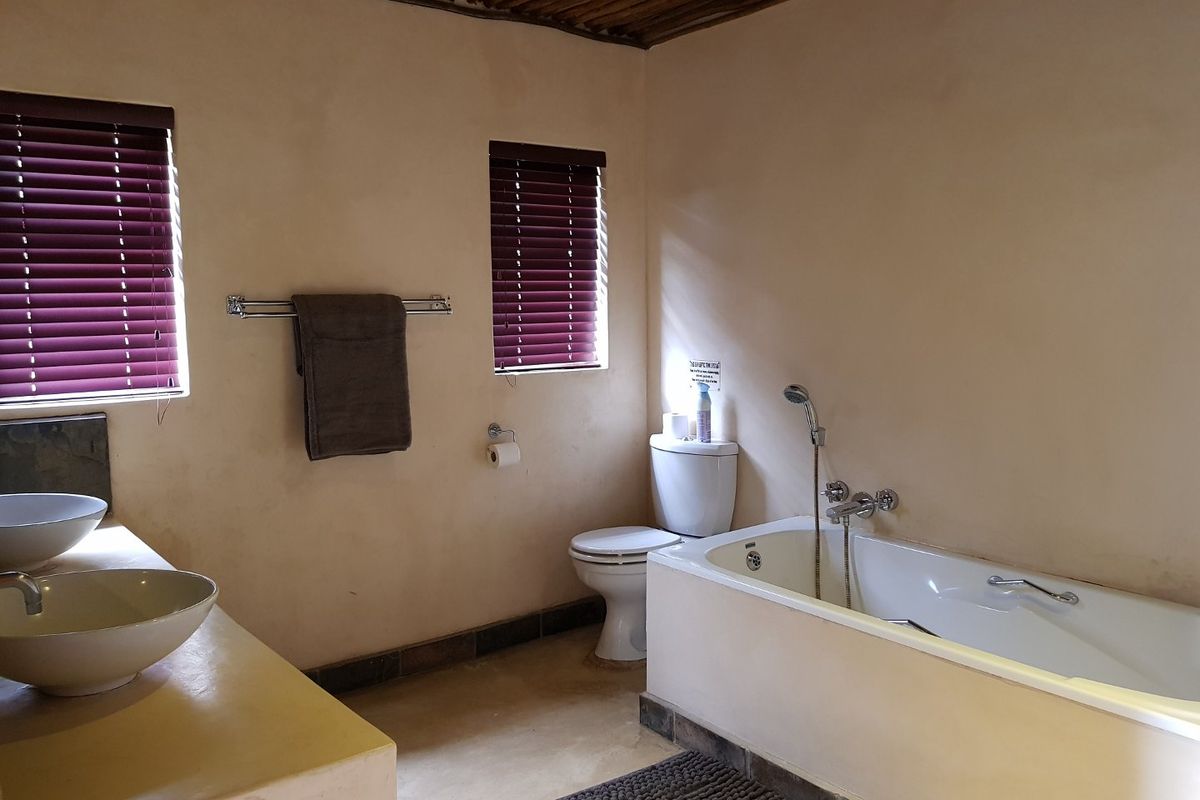 A rustic-style bathroom featuring a built-in vanity with dual vessel sinks, a standard bathtub with shower mixer, and a toilet.