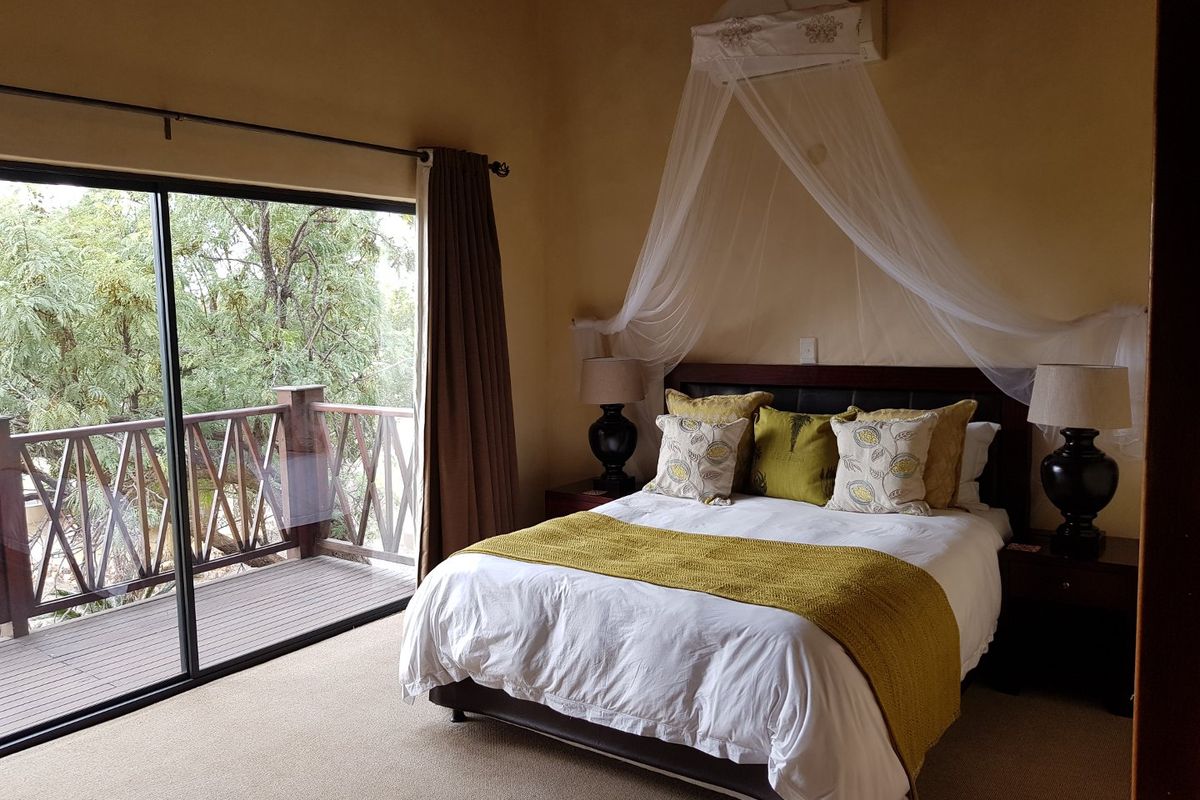 A comfortable bedroom featuring neutral carpeting, wall-mounted air conditioning, and large sliding glass doors that open onto a private wooden balcony.