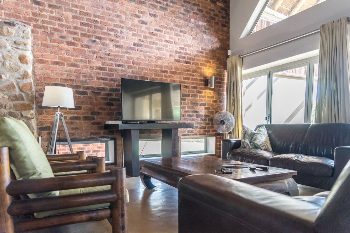 Spacious living room featuring a striking exposed brick feature wall, high vaulted ceilings, and large windows that provide ample natural light.