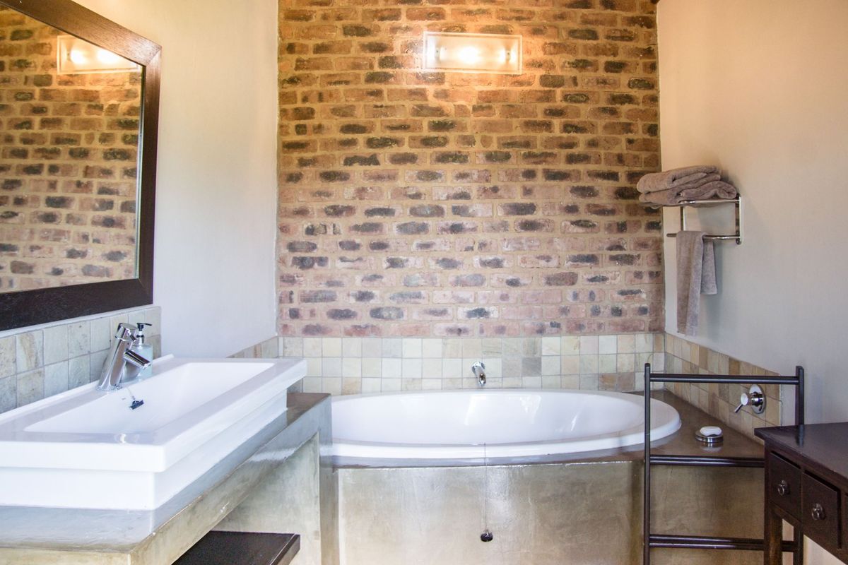 A bathroom featuring a built-in bathtub with a concrete surround, a modern vanity basin, and a rustic exposed brick feature wall.
