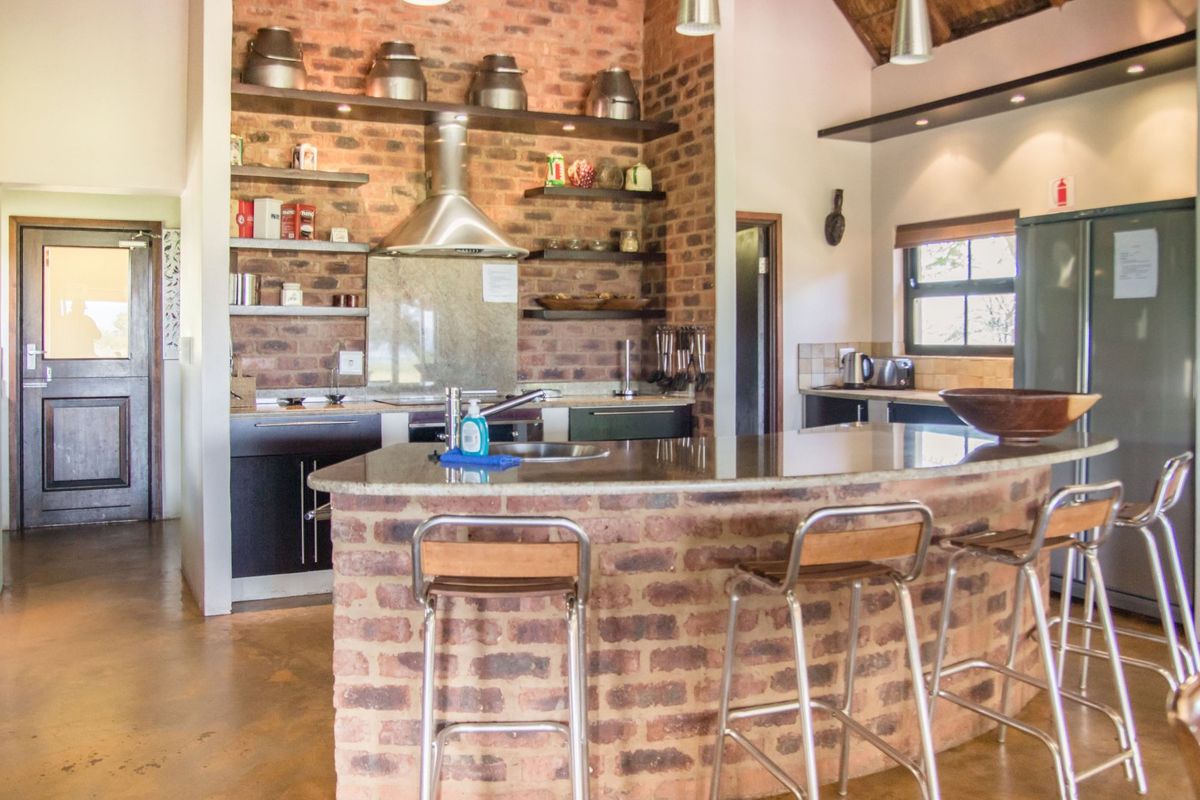A rustic kitchen featuring exposed brick walls, a curved brick breakfast bar with granite countertop, stainless steel extractor fan, and open shelving.