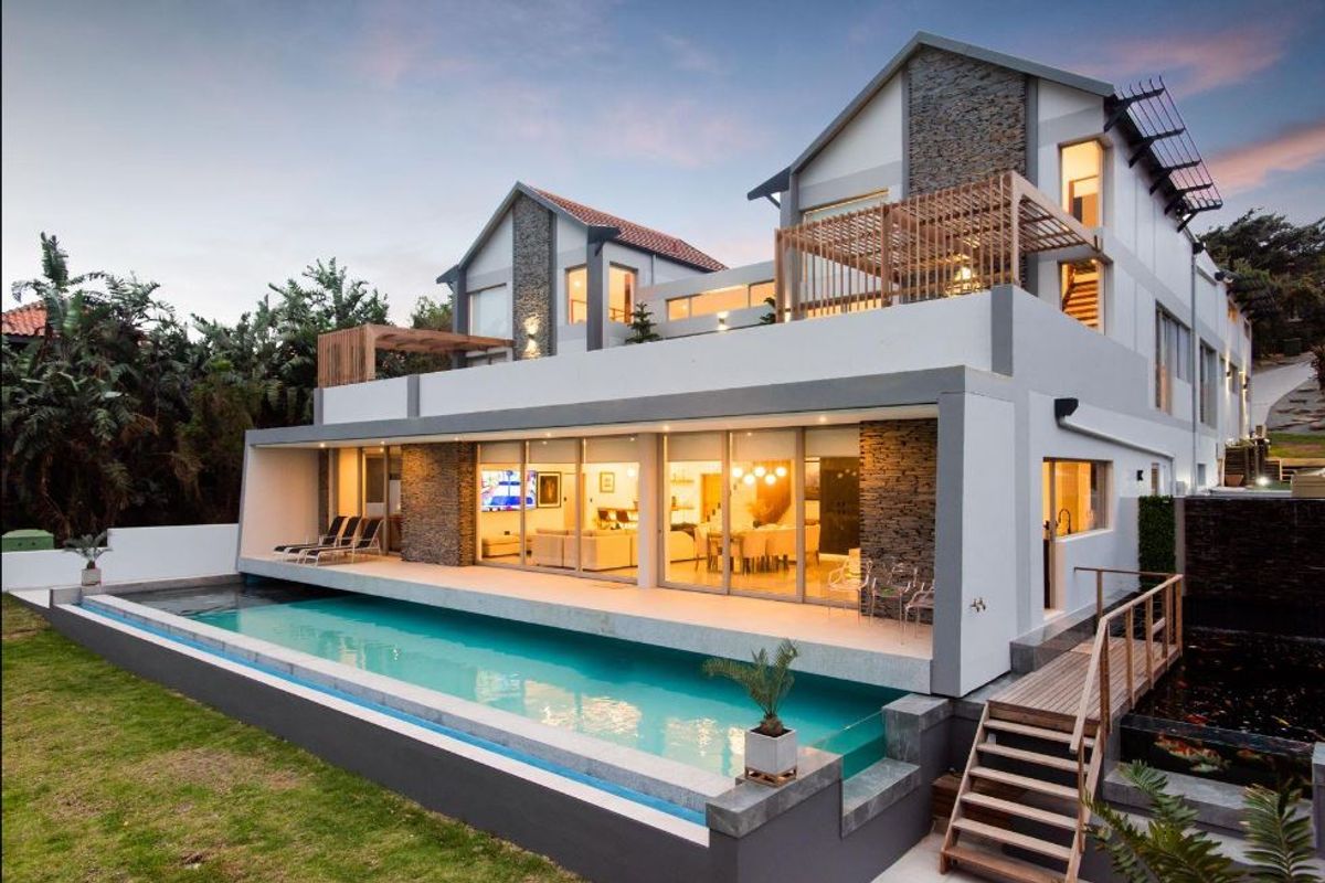 Modern multi-level residence featuring a swimming pool, stone-clad facade, timber pergola, and expansive glass sliding doors opening to a rear patio area.
