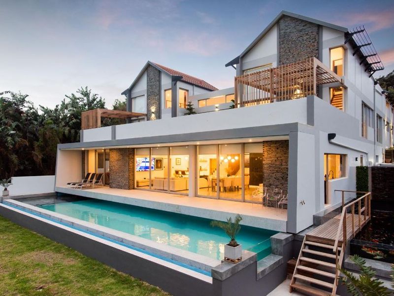 Modern multi-level residence featuring a swimming pool, stone-clad facade, timber pergola, and expansive glass sliding doors opening to a rear patio area.