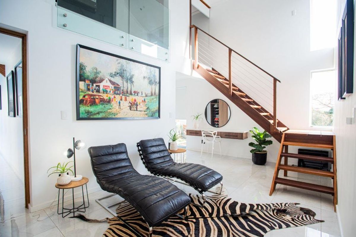 Modern living area featuring a striking timber staircase with glass balustrade, polished tiled floors, and a sleek floating wall-mounted desk.