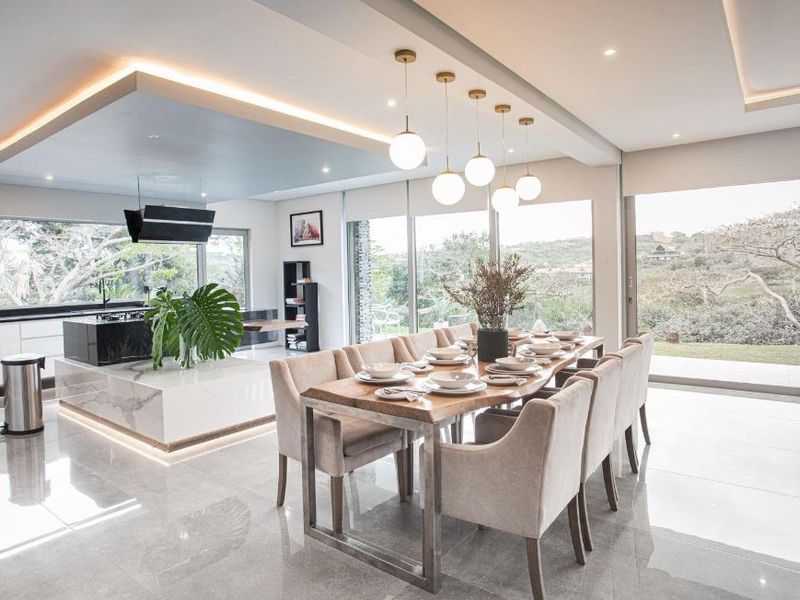 Modern open-plan living and dining area featuring a sleek kitchen island with marble finishes, recessed lighting, and expansive sliding glass doors overlooking the landscape.