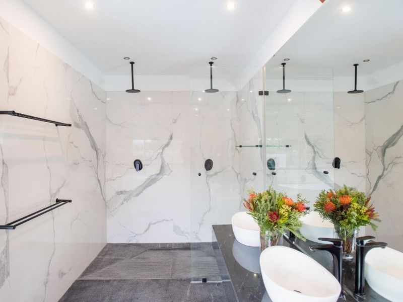 Modern bathroom featuring a spacious walk-in shower with dual rainfall heads, marble-look tiling, dual vessel sinks, and sleek black matte fixtures.