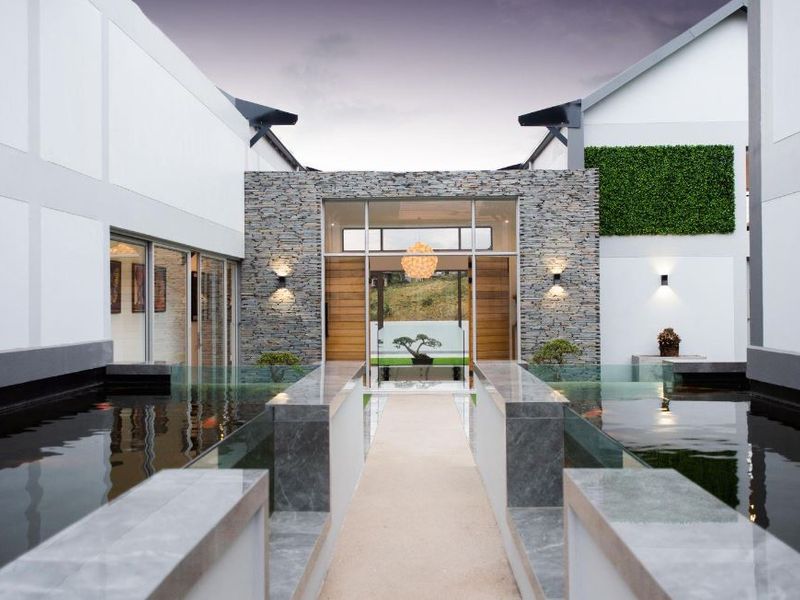 A modern architectural entrance featuring a central walkway flanked by reflective water features, stone-clad walls, and contemporary exterior lighting.