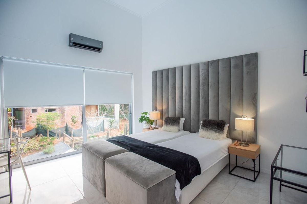 Modern bedroom featuring tiled flooring, a wall-mounted air conditioning unit, and large glass sliding doors with roller blinds providing natural light.