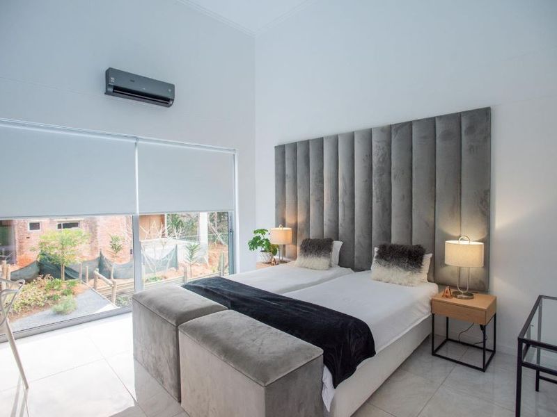 Modern bedroom featuring tiled flooring, a wall-mounted air conditioning unit, and large glass sliding doors with roller blinds providing natural light.
