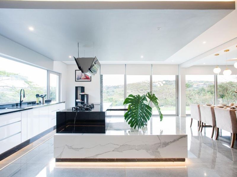 Modern open-plan kitchen and dining area featuring a large marble-topped island, gas hob, sleek cabinetry, and expansive windows with scenic views.