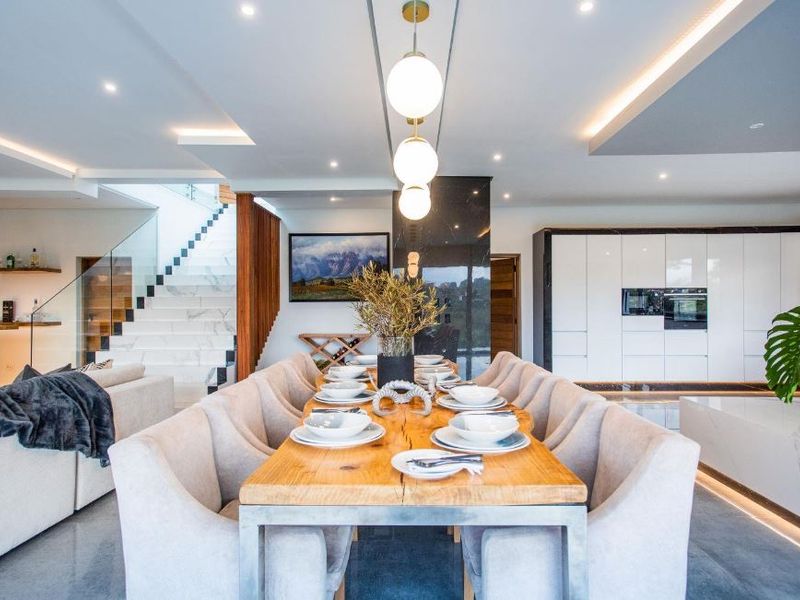 A modern open-plan living and dining area featuring high-end finishes, a striking marble staircase with glass balustrade, and sleek integrated kitchen cabinetry.