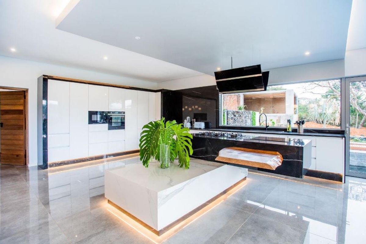 Modern luxury kitchen featuring high-gloss cabinetry, a striking marble island, black stone countertops, integrated appliances, and ambient recessed lighting.