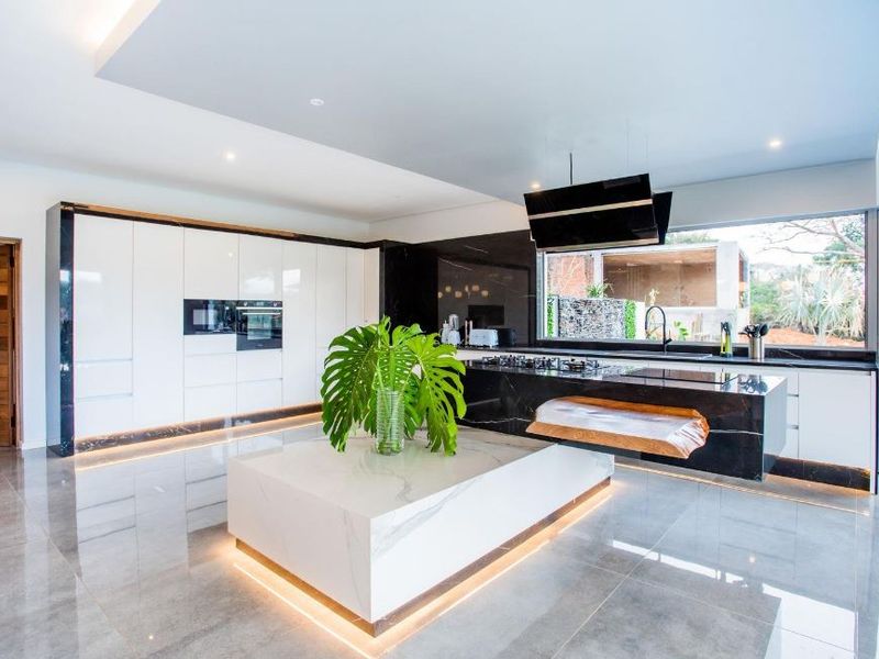 Modern luxury kitchen featuring high-gloss cabinetry, a striking marble island, black stone countertops, integrated appliances, and ambient recessed lighting.
