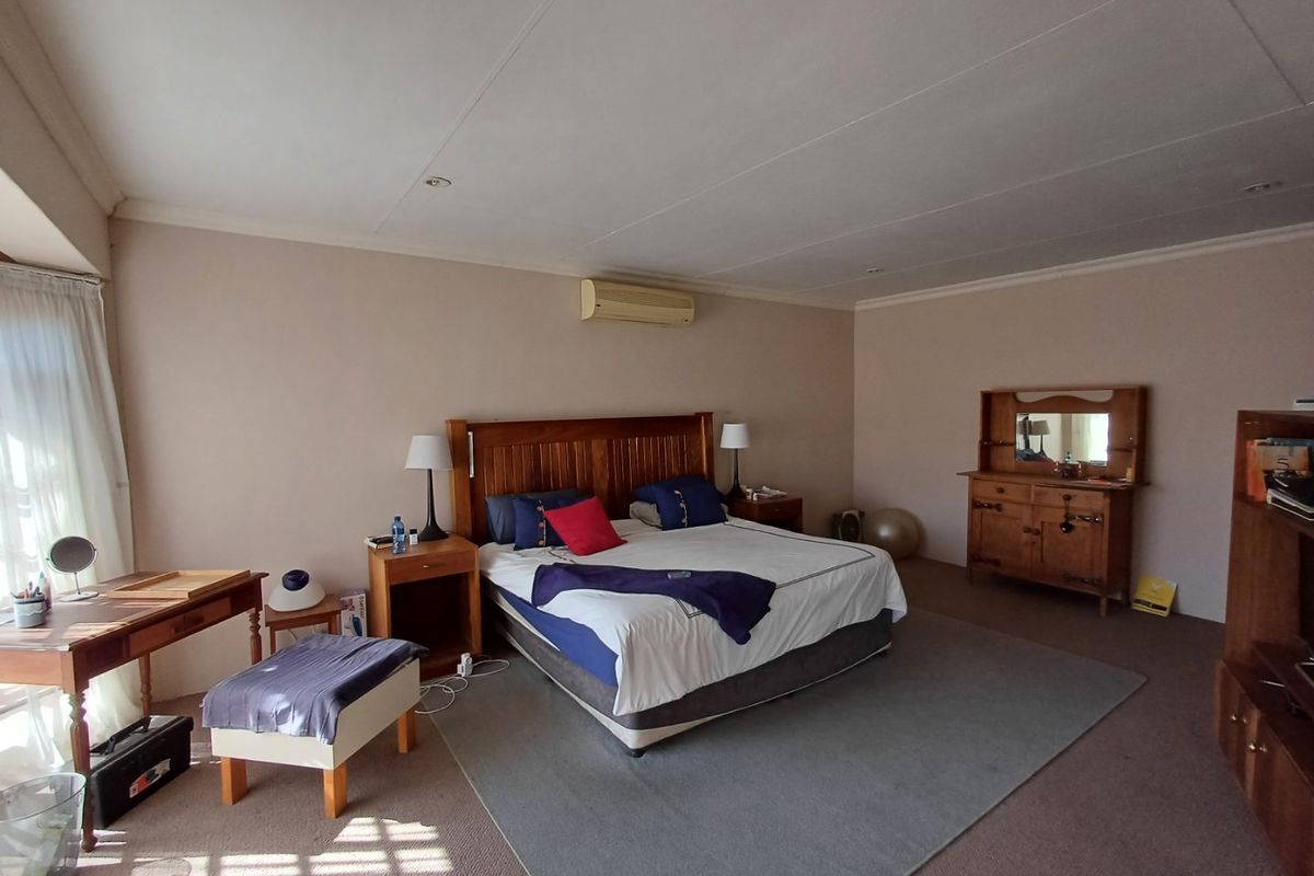 Spacious bedroom featuring neutral walls, carpeted flooring, and a wall-mounted air conditioning unit.