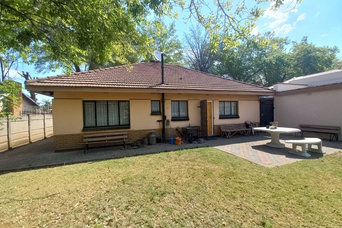 Rear view of the house featuring a paved patio area, tiled roof, and established garden space.