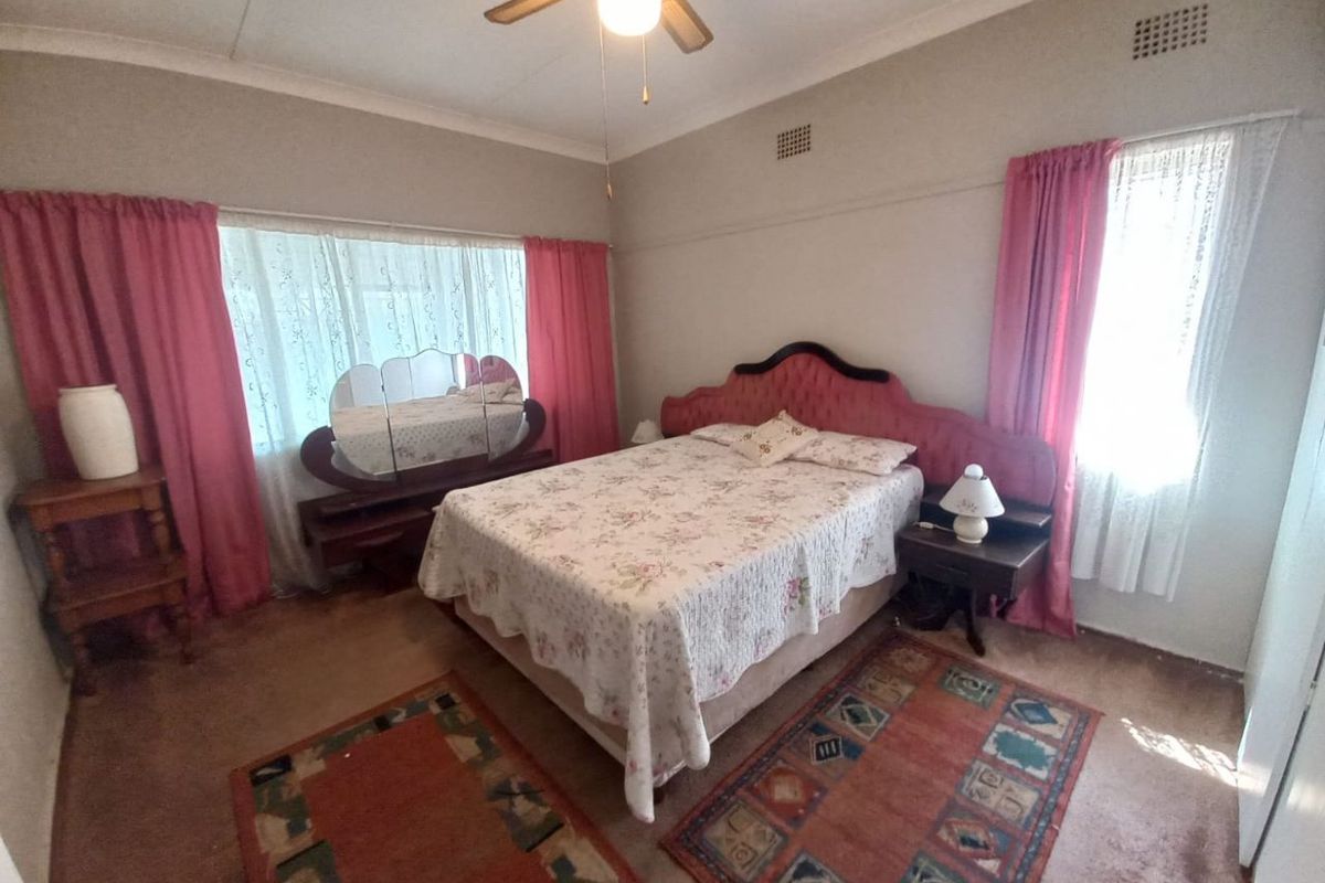 A spacious bedroom featuring large windows with curtains, a ceiling fan, and carpeted flooring.