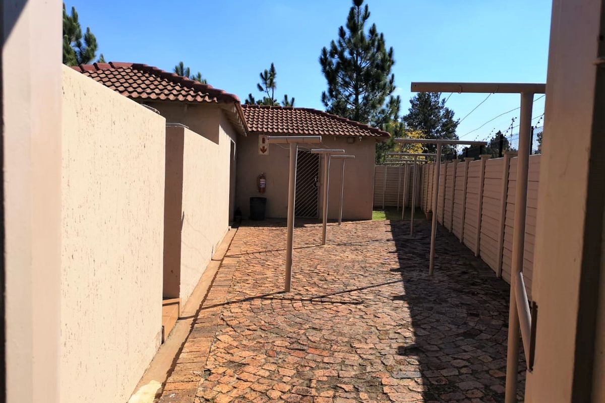 A paved outdoor utility area featuring fixed metal washing lines, enclosed by boundary walls and providing access to the rear of the property.