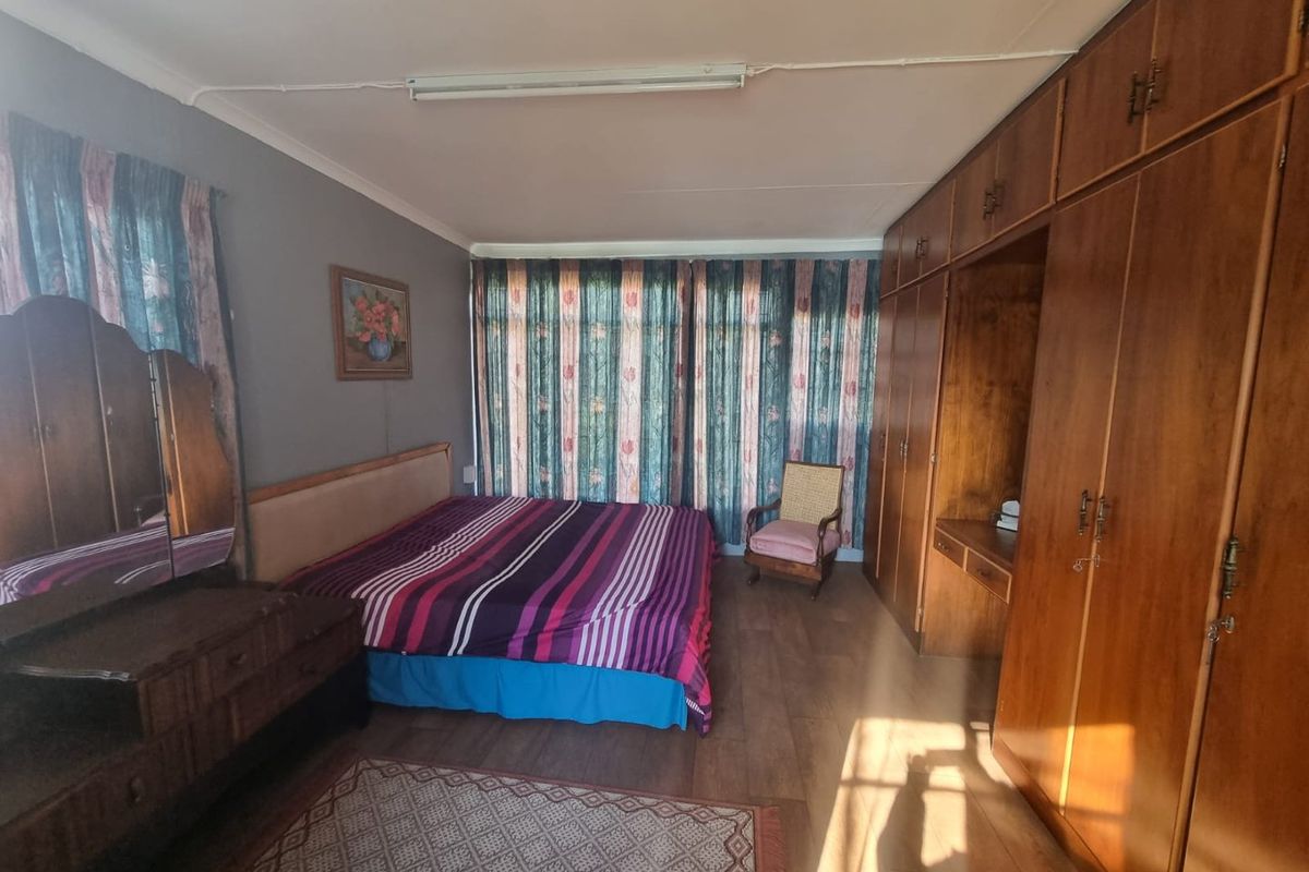 Spacious bedroom featuring extensive built-in wooden cabinetry, laminate flooring, and large windows with curtain treatments.