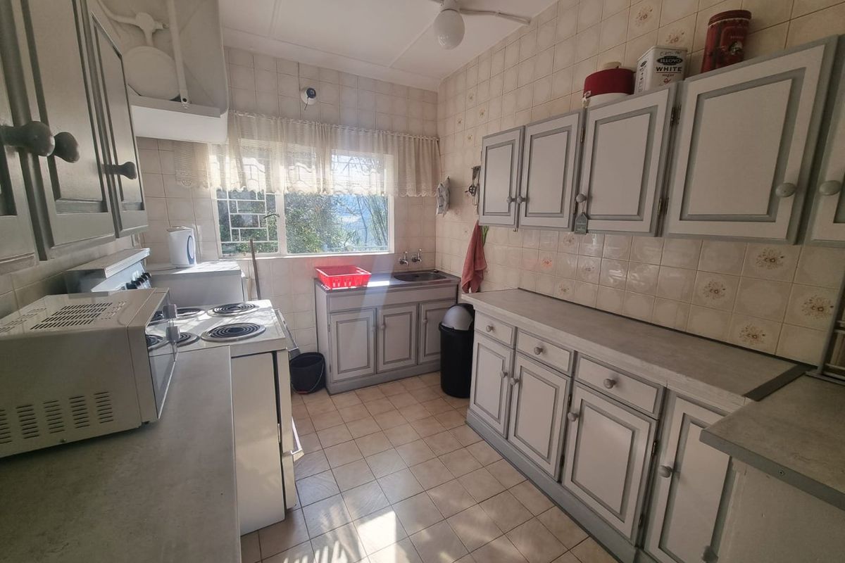 A functional kitchen featuring tiled walls, ample built-in cabinetry, a stainless steel sink, and a freestanding electric stove.